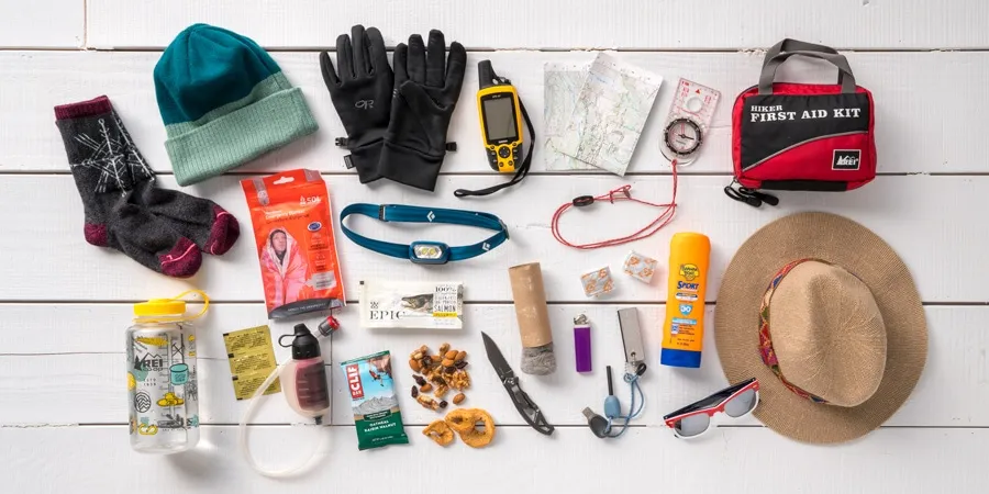 Essential hiking gear laid out including backpack, water bottles, hiking boots, and safety equipment